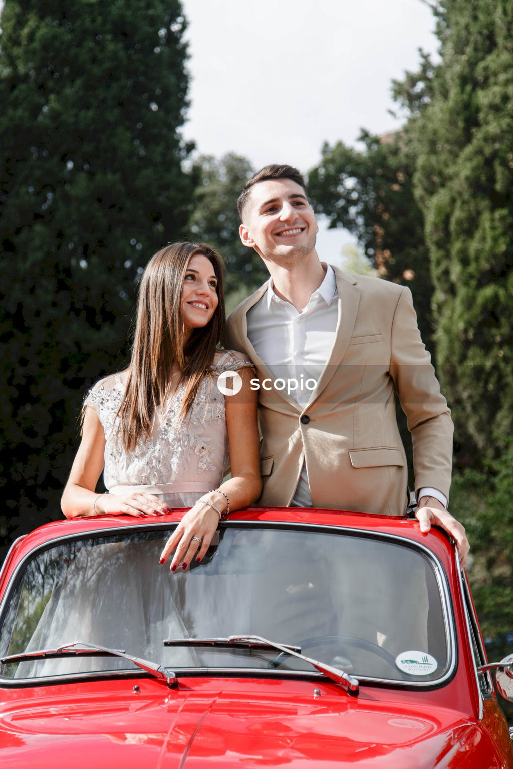 Man in brown suit jacket hugging woman in white floral dress