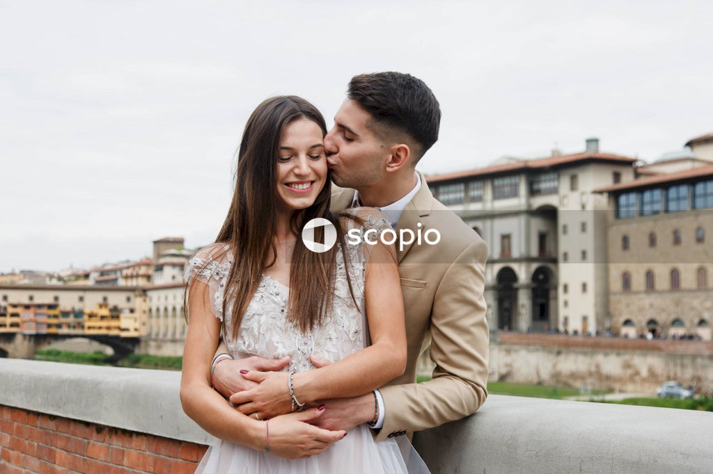 Man in brown suit jacket hugging woman in white floral lace dress