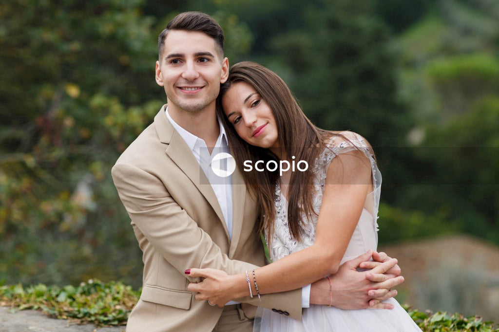 Man in brown suit jacket hugging woman in white sleeveless dress