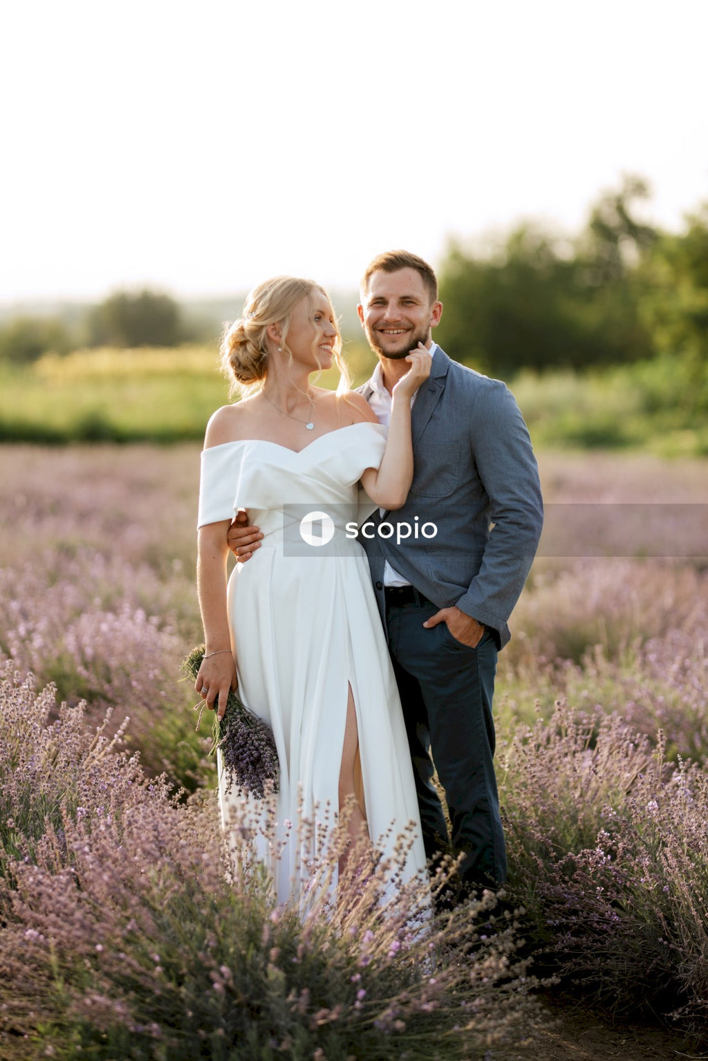 Man in gray suit jacket hugging woman in white dress on green grass field