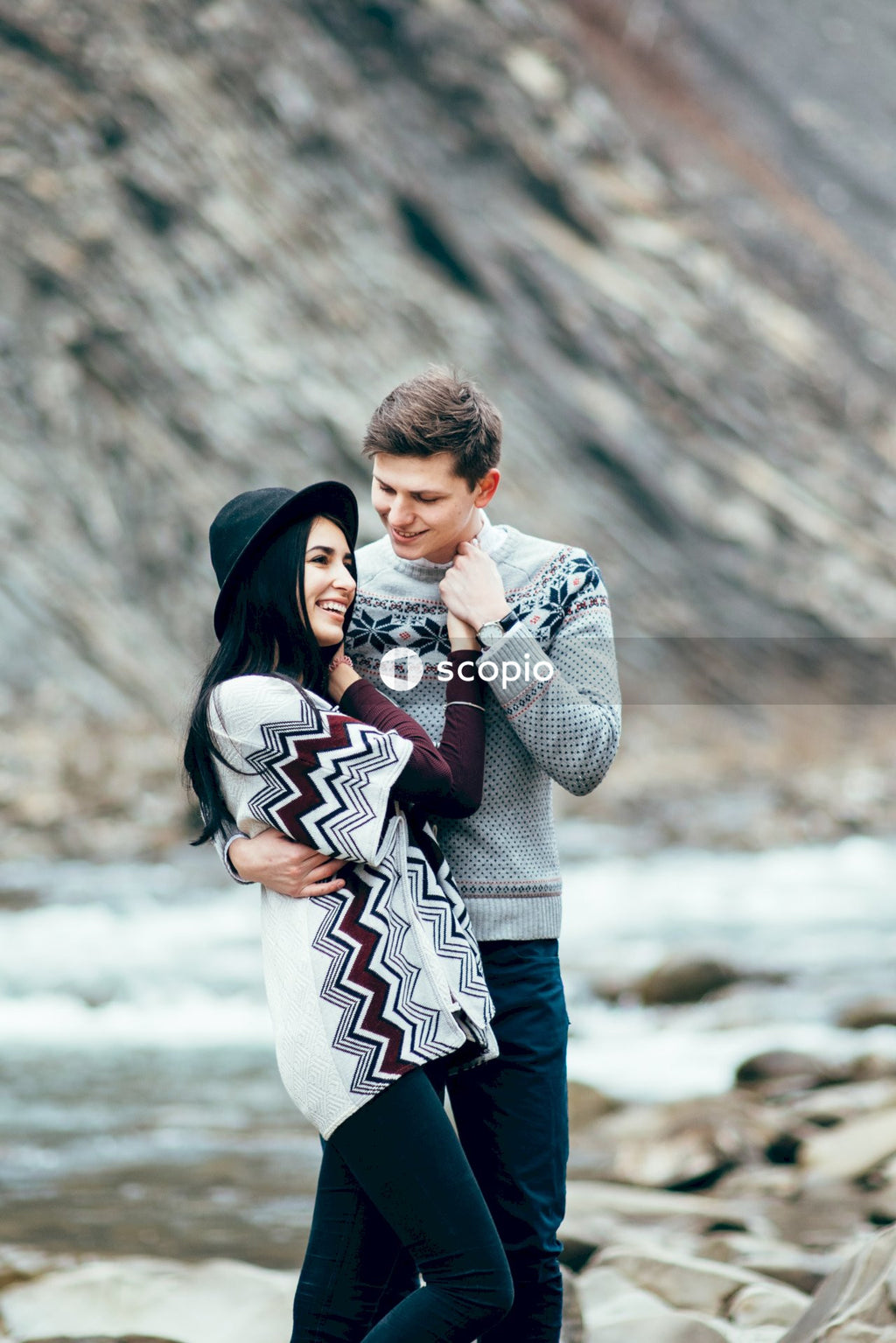 Man in gray sweater hugging woman in white and blue dress