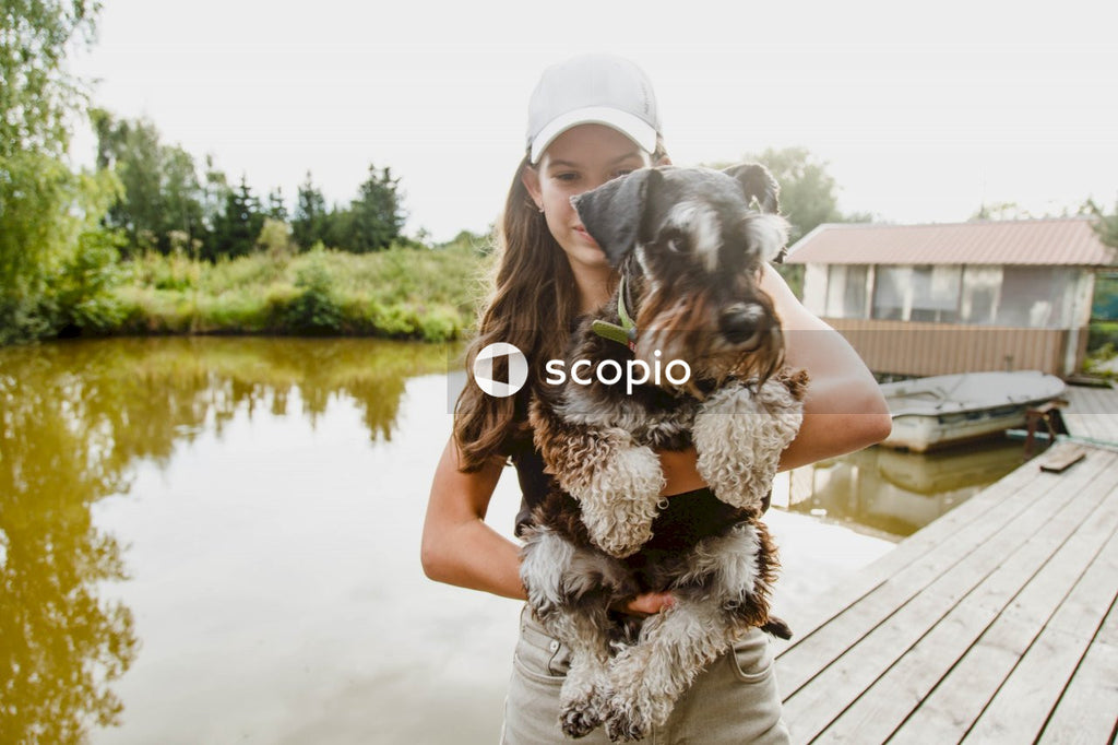 Man in gray t-shirt hugging black and brown short coated small dog