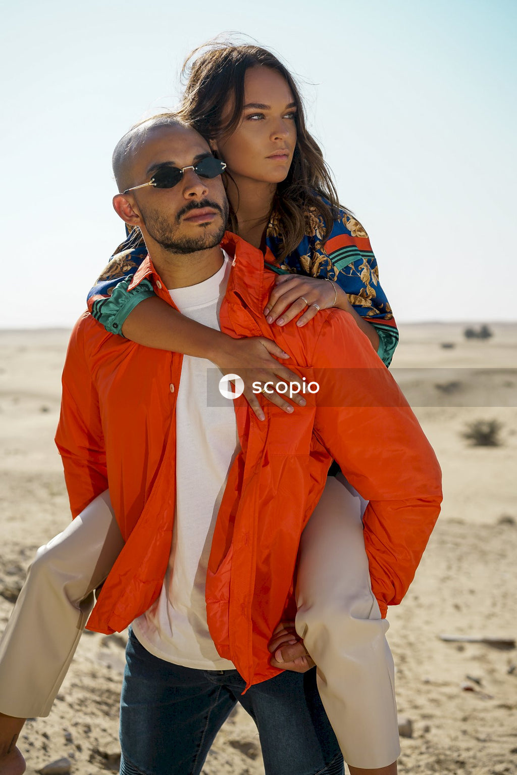 Man in orange robe hugging woman in blue and brown floral dress on beach