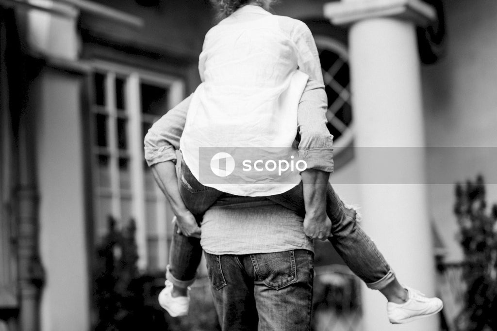 Grayscale photo of man holding woman on his back