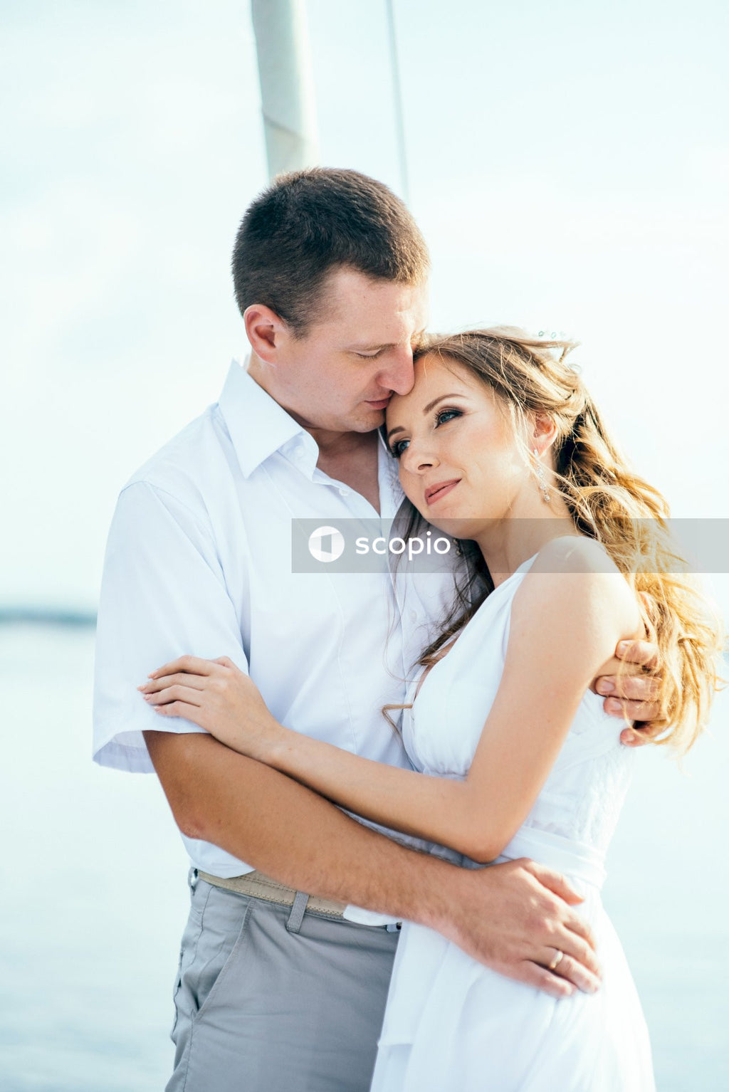 Man in white dress shirt hugging woman in white sleeveless dress
