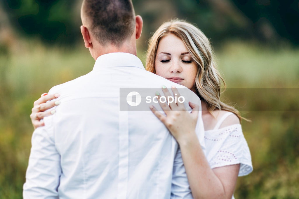 Man in white dress shirt hugging woman in white sleeveless dress