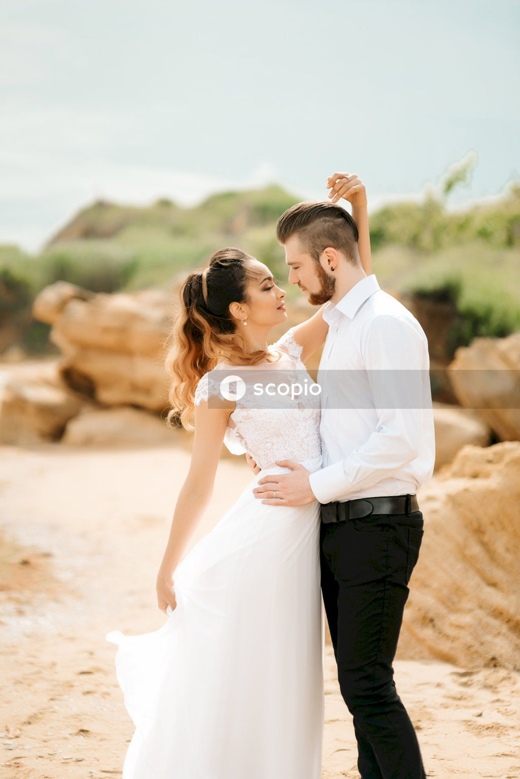 Man in white dress shirt kissing woman in white dress shirt on brown sand