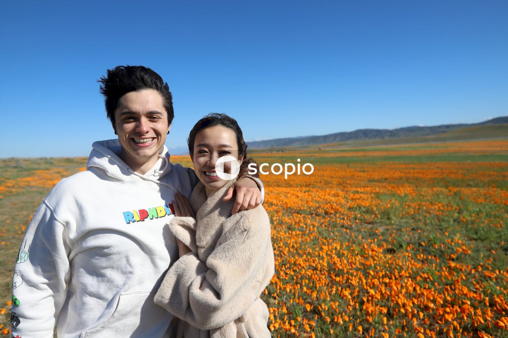 Man in white jacket hugging woman in beige coat on yellow flower field