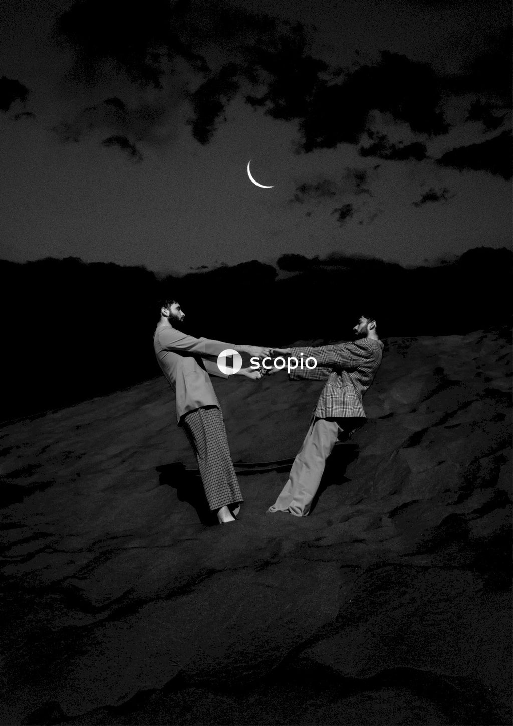 Grayscale photo of two in gray suits holding hands standing under crescent moon