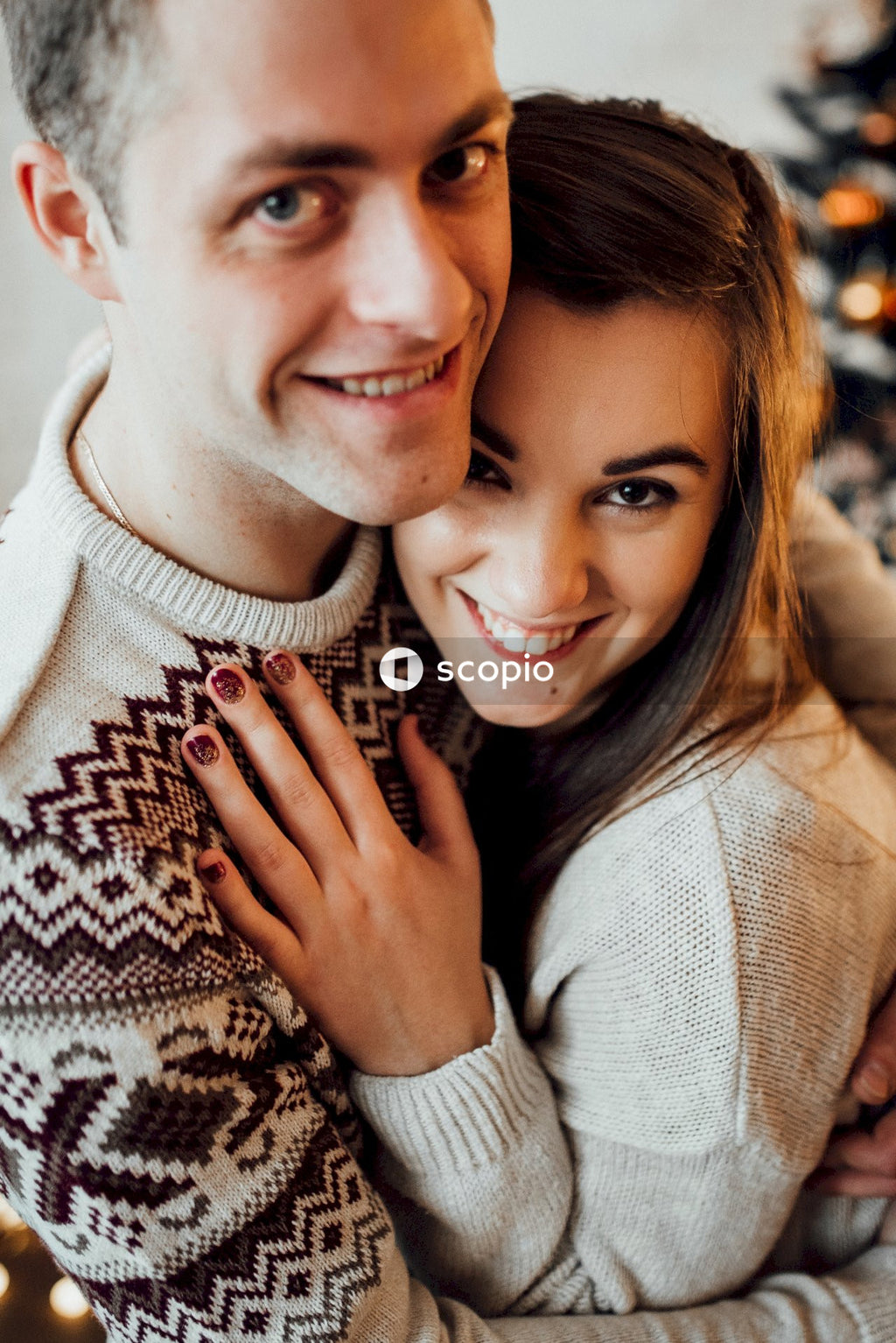 Man in white sweater hugging woman in brown and black sweater