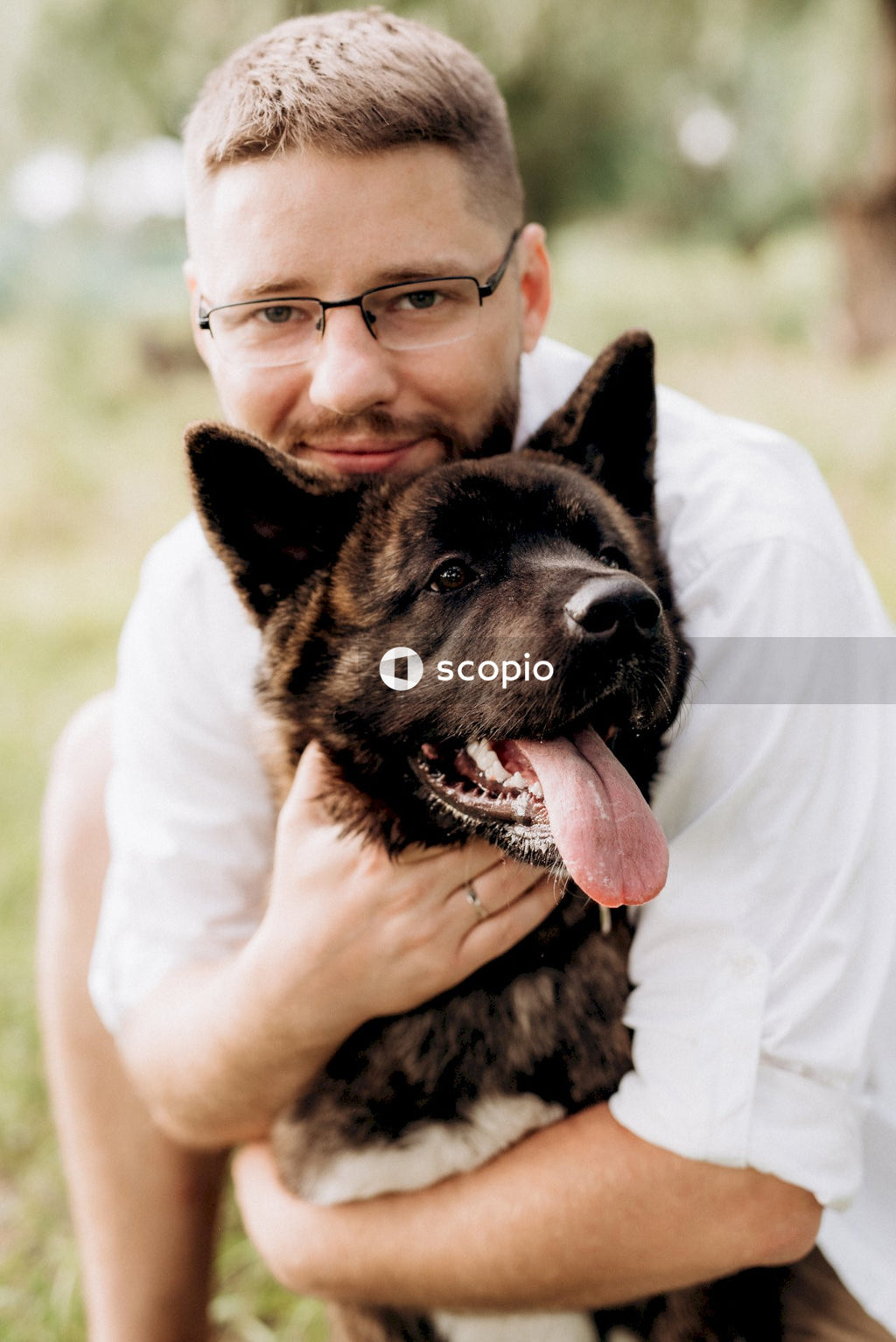 Man in white t-shirt hugging black and brown short coated dog