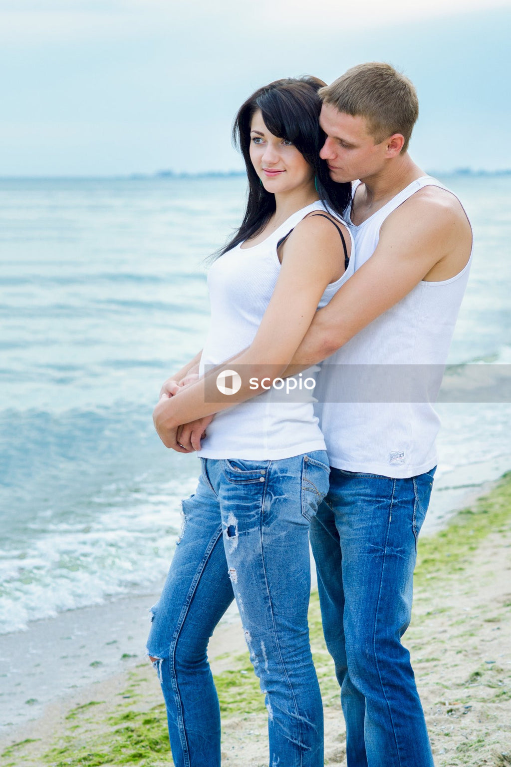 Man in white tank top and blue denim jeans hugging woman in white tank top on near near near near