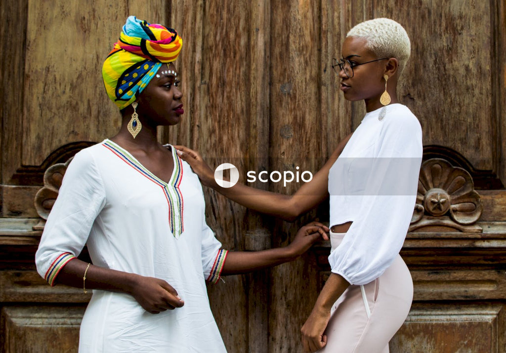 Woman with headwrap and a woman with short hair standing beside wooden door