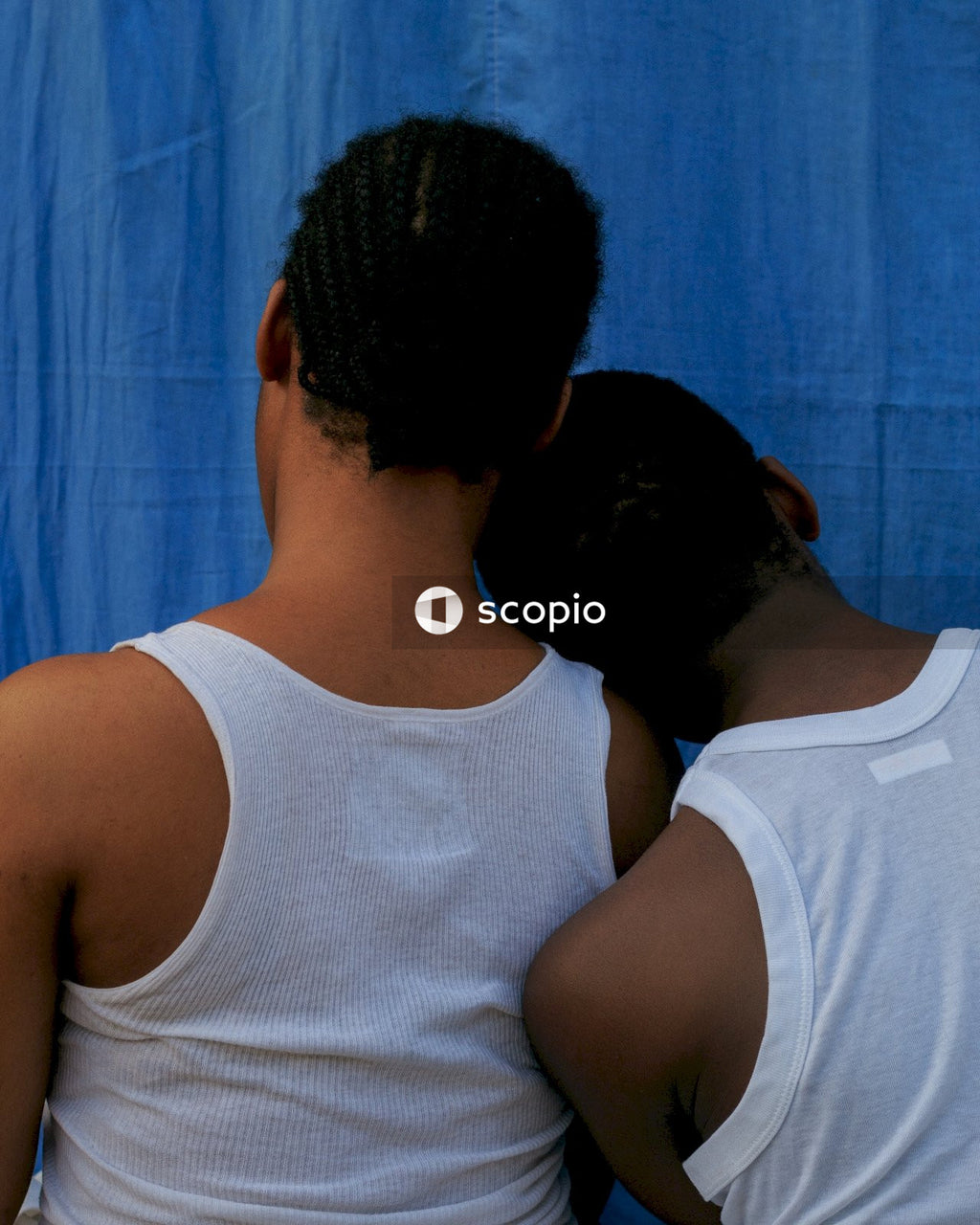 Back view of man leaning his head on another man's shoulder against blue background
