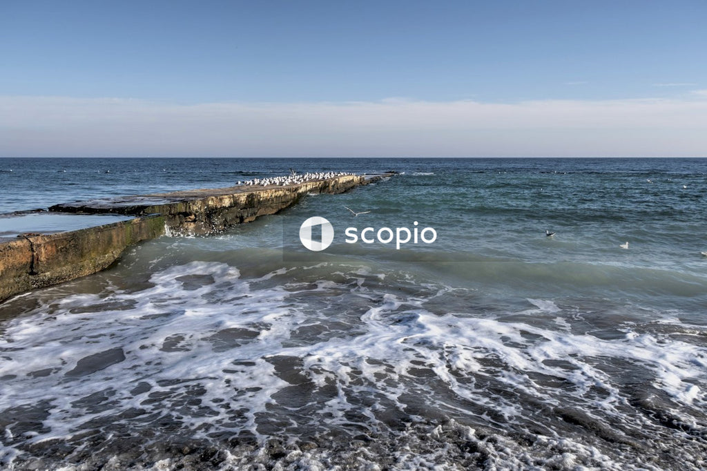 Ocean waves crashing on rocks under blue sky