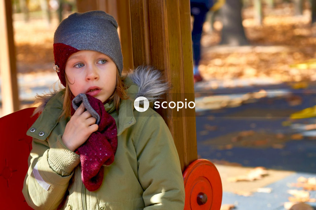 Offended frightened child in a jacket and a hat on an autumn playground