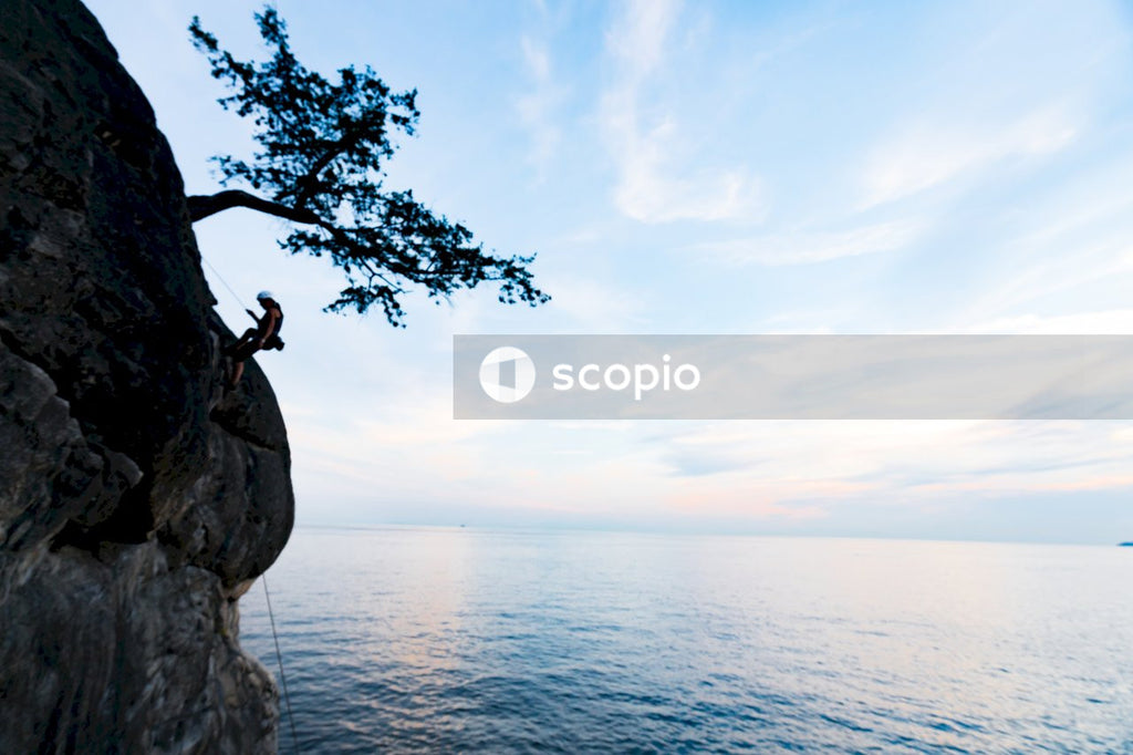 Person climbing rocky cliff beside body of water