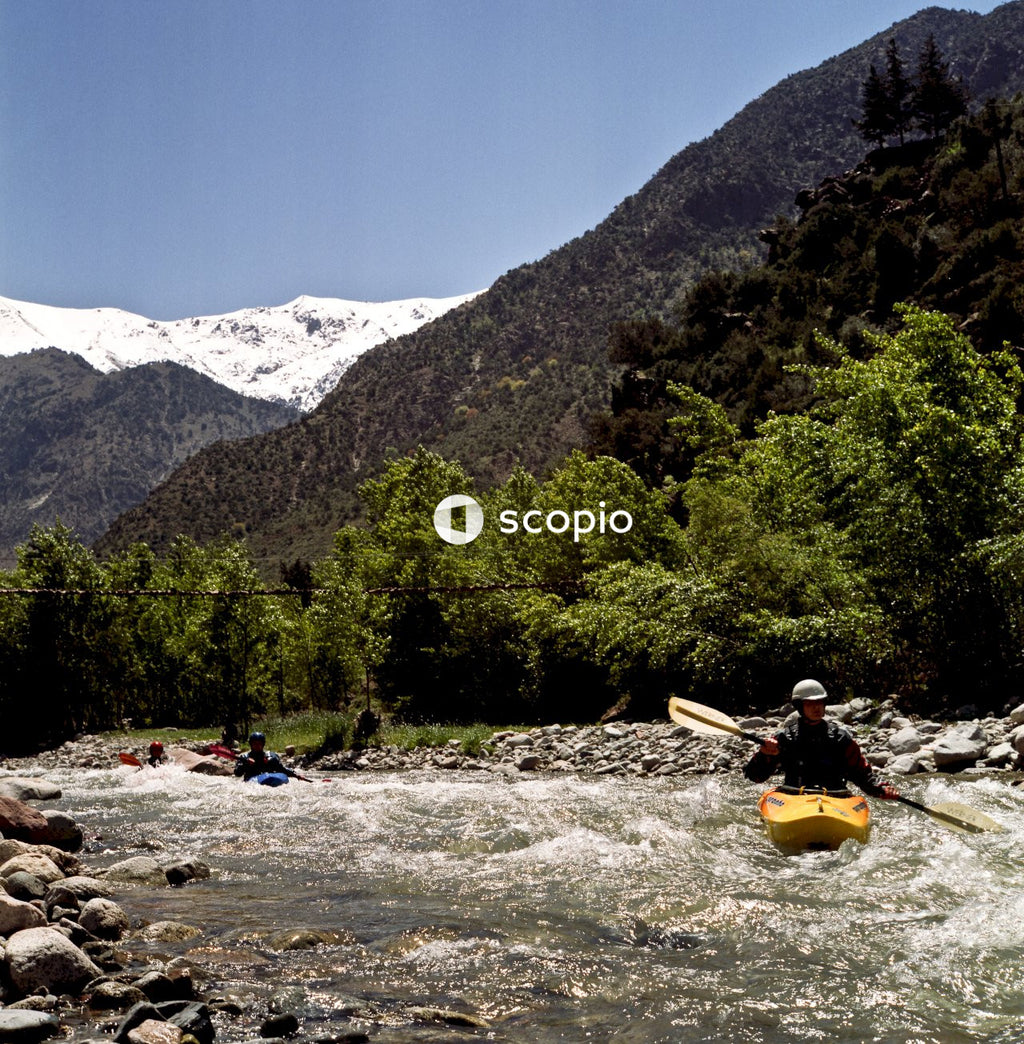 Person riding yellow kayak on river near green trees and mountains