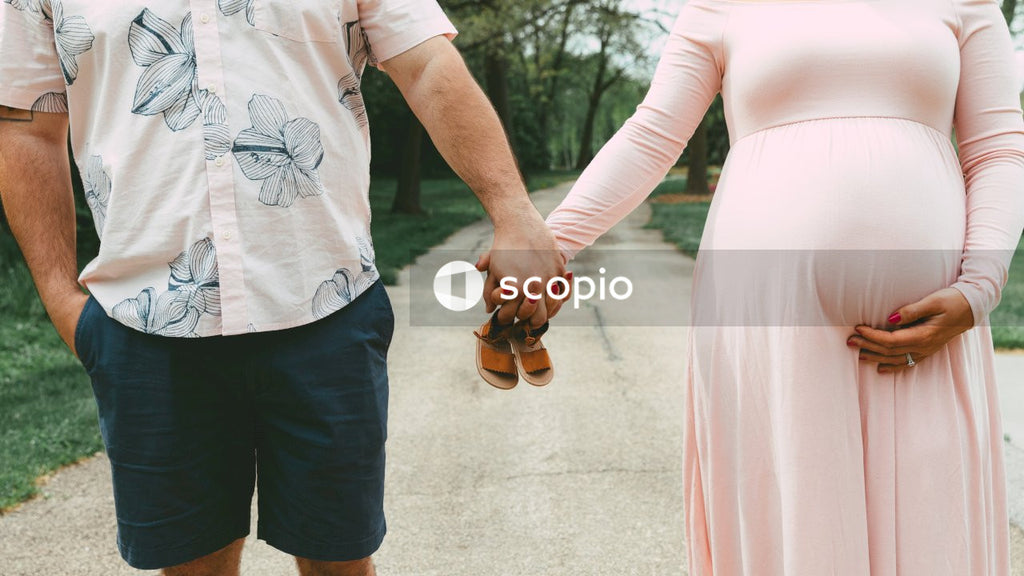 Pregnant woman and man holding hands and holding baby shoes outdoor