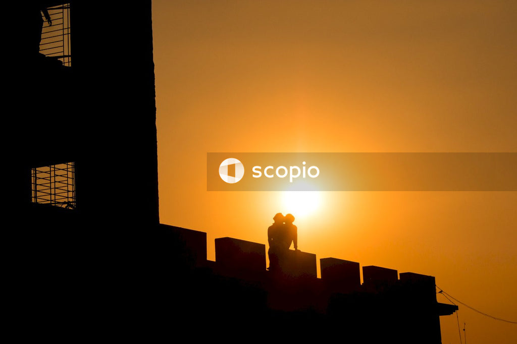 Silhouette of two people kissing on top of building during sunset