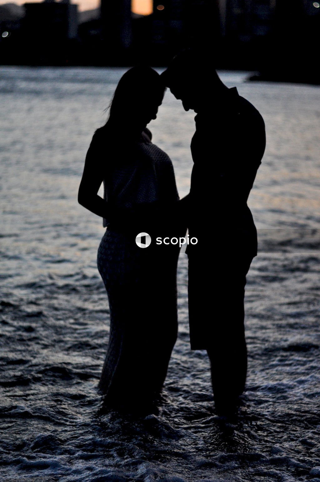 Silhouette of pregnant woman and a man standing on shallow water during sunset