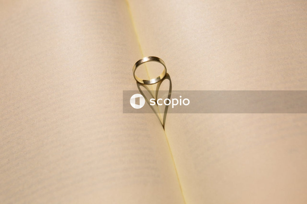 Silver ring on white book page that casts a heart shaped shilouhette