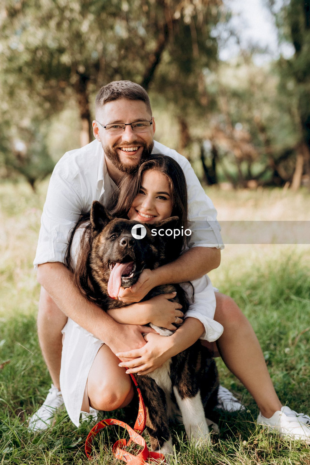 Smiling woman in white t-shirt hugging black and brown short coated dog on green grass
