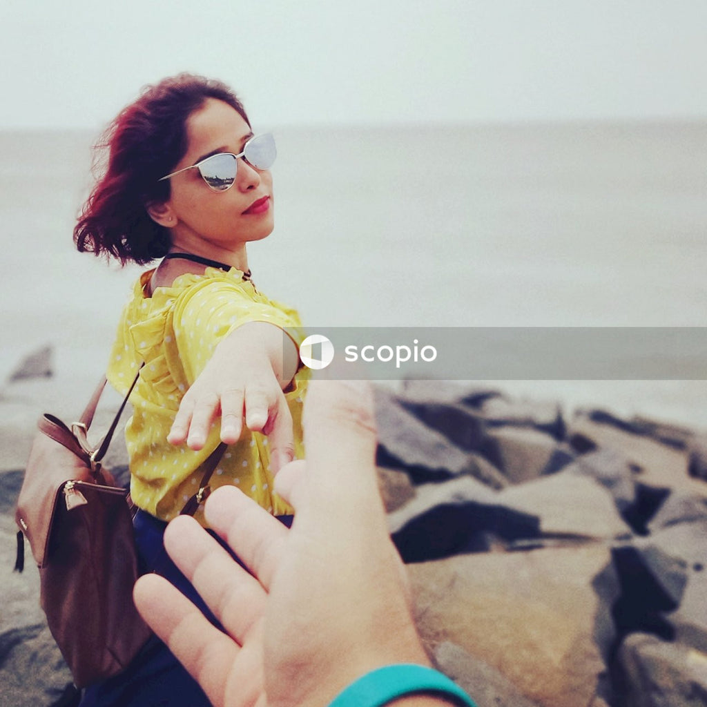 South Asian woman in yellow top reaching out a hand on seashore
