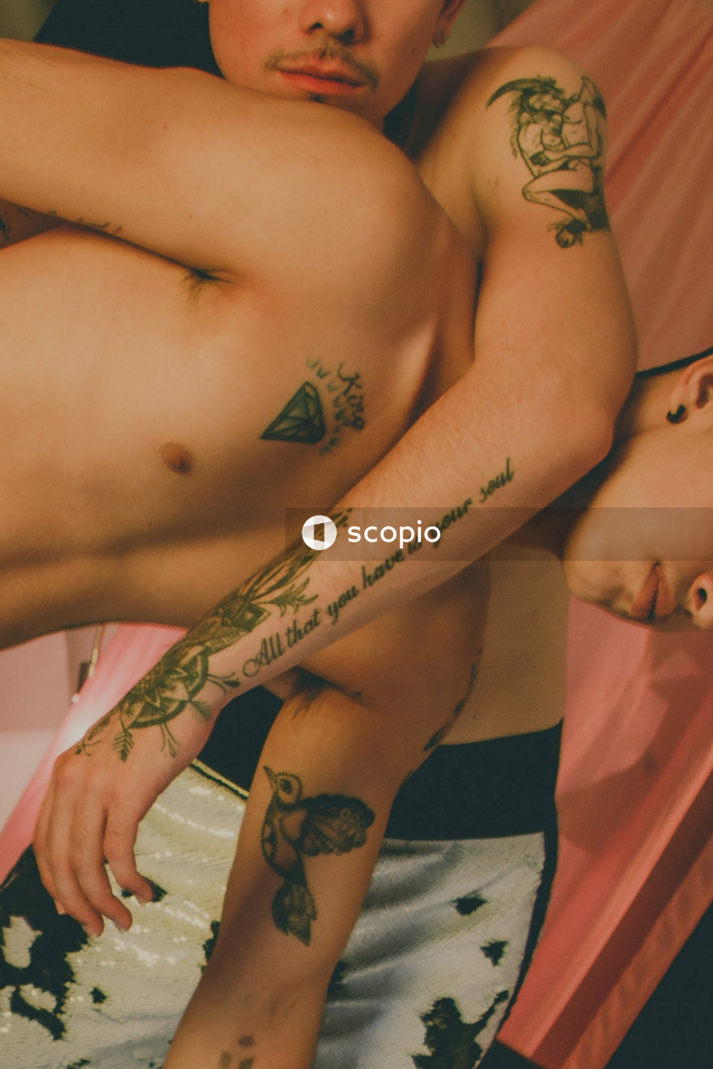 Two tattooed topless men hugging each other