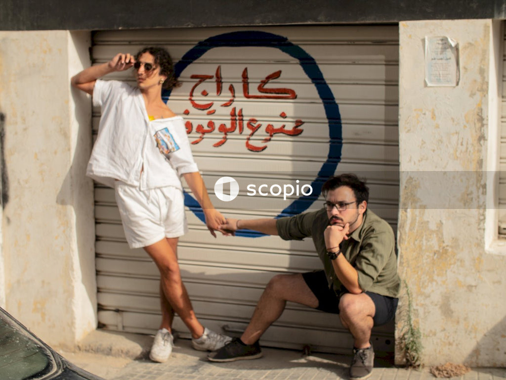 Two men holding hands in front of "No Parking" sign in Arabic