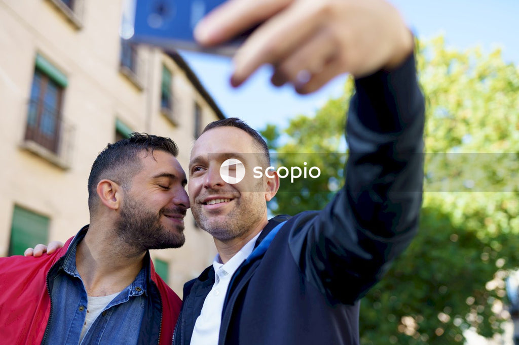 Two men taking selfie beside a building and tree