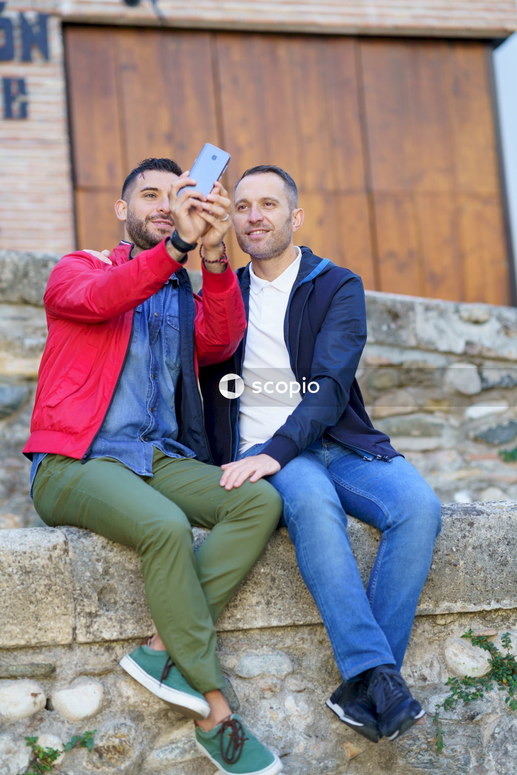 Two sitting side by side men taking selfie