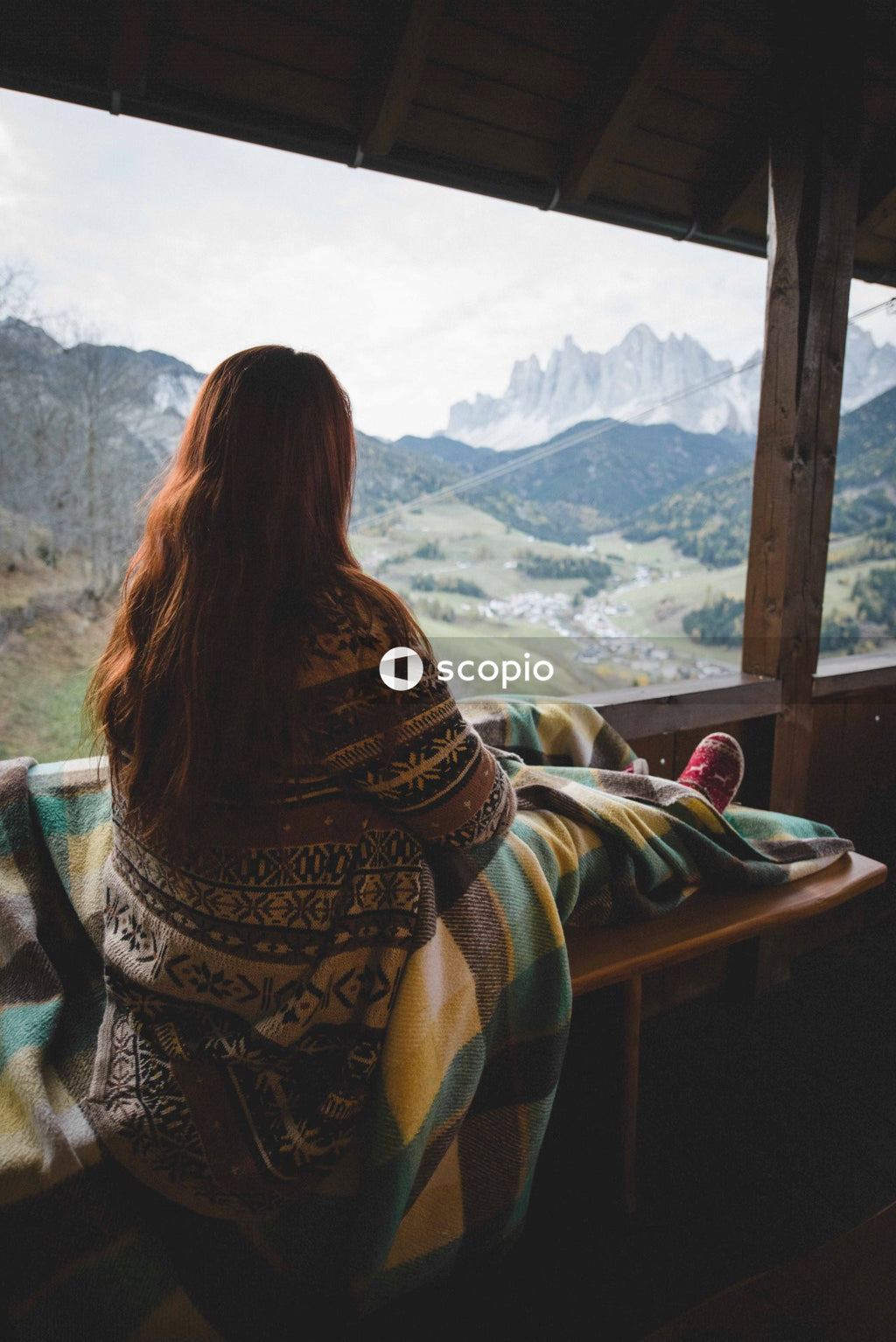 Woman in a sweater sitting on brown wooden bench in a balcony overlooking mountains