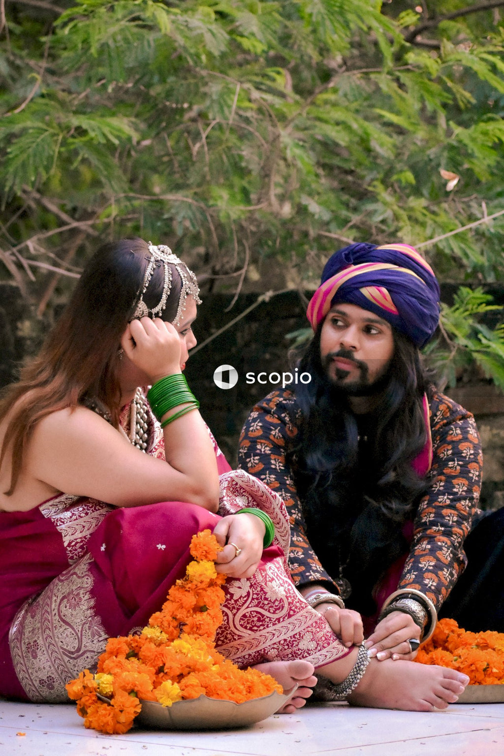 Indian man wearing turban sitting beside woman in colorful dress on floor outdoor