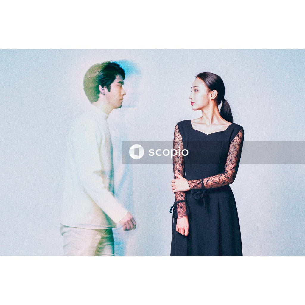 Man in light outfit standing beside woman in dark dress against light background