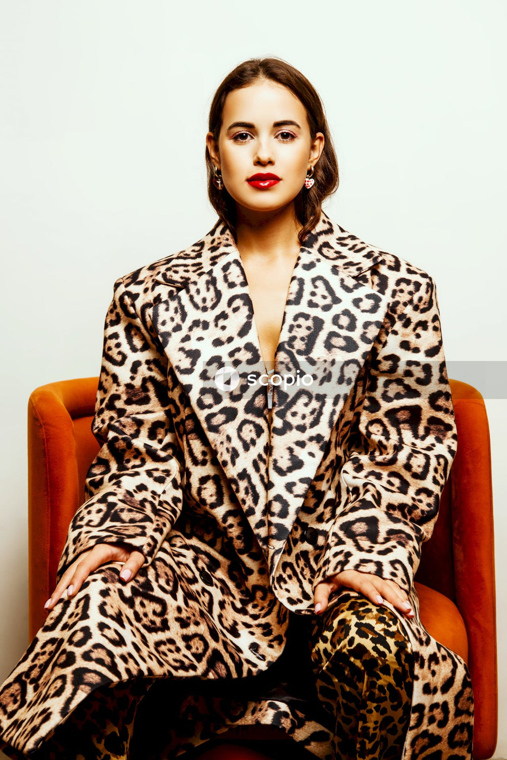 Woman in black and white leopard print robe sitting on orange leather armchair