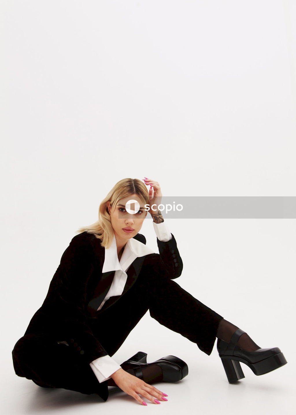 Woman in black blazer and black pants sitting on white floor