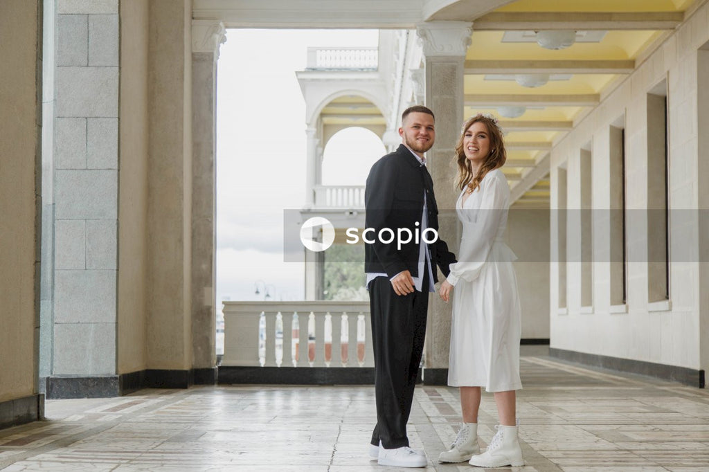Woman in black blazer standing on white floor tiles with a man