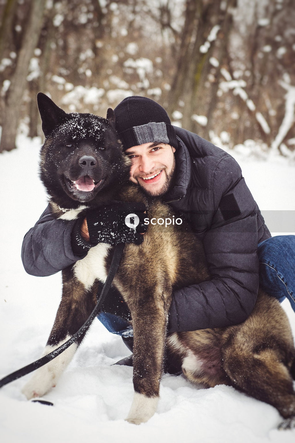 Woman in black jacket hugging black and brown dog on snow covered ground