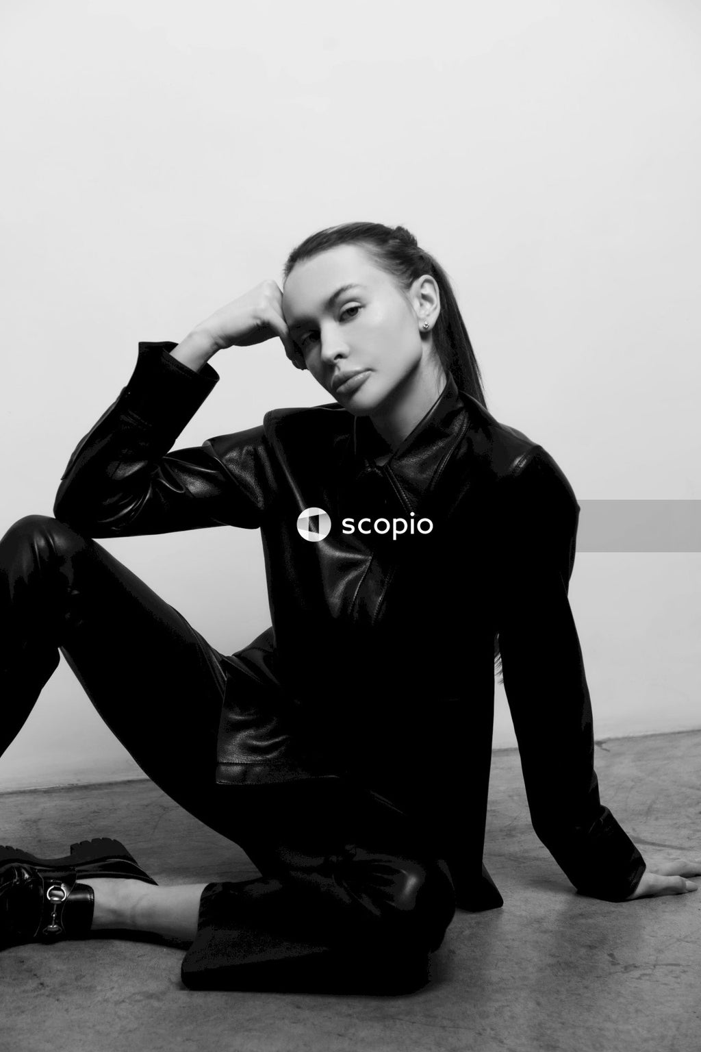 Woman in black leather jacket and black pants sitting on ground