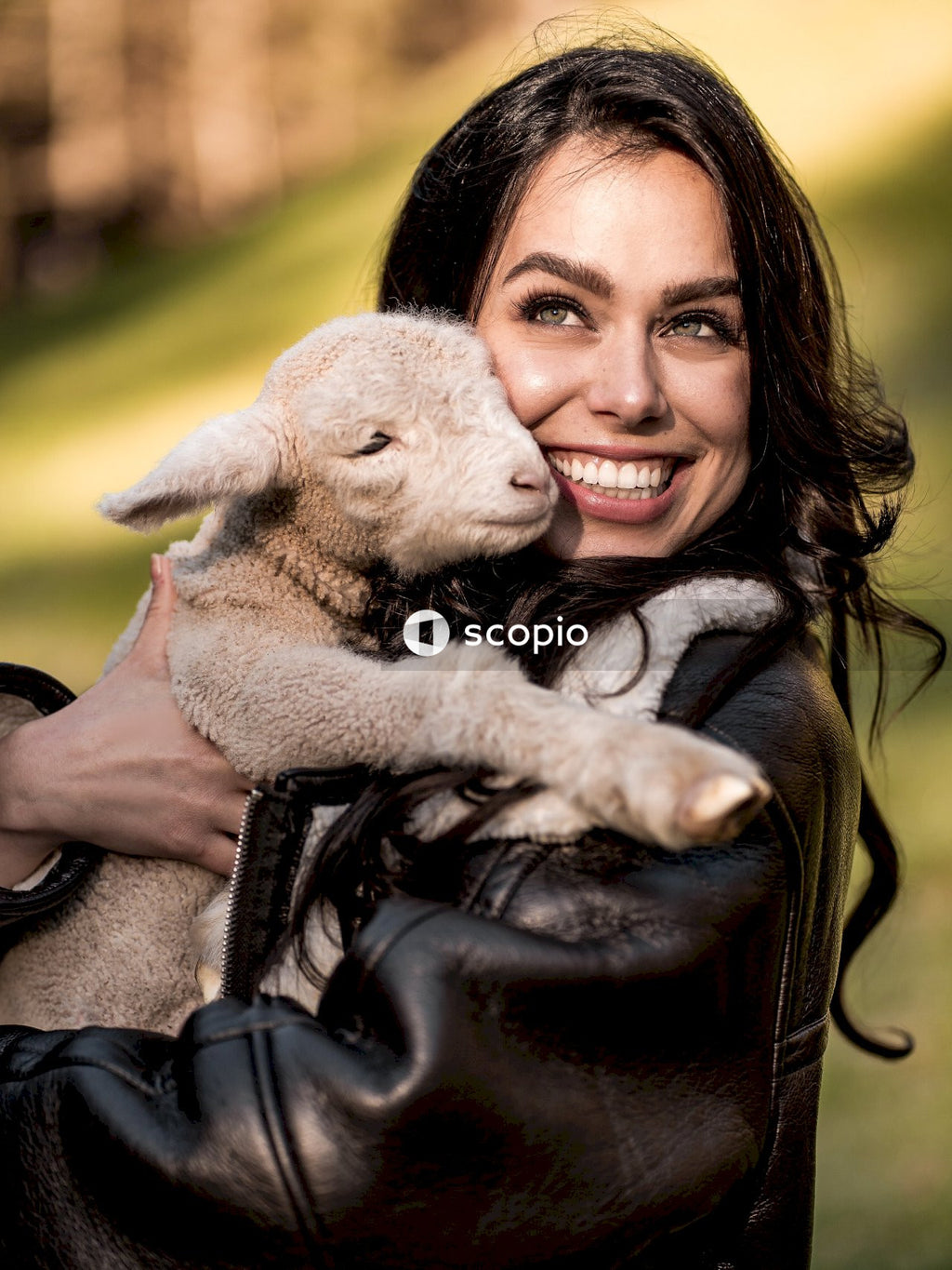 Woman in black leather jacket hugging white sheep