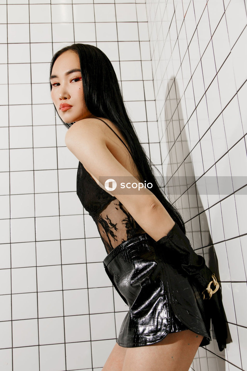 Woman in black leather jacket leaning on white wall