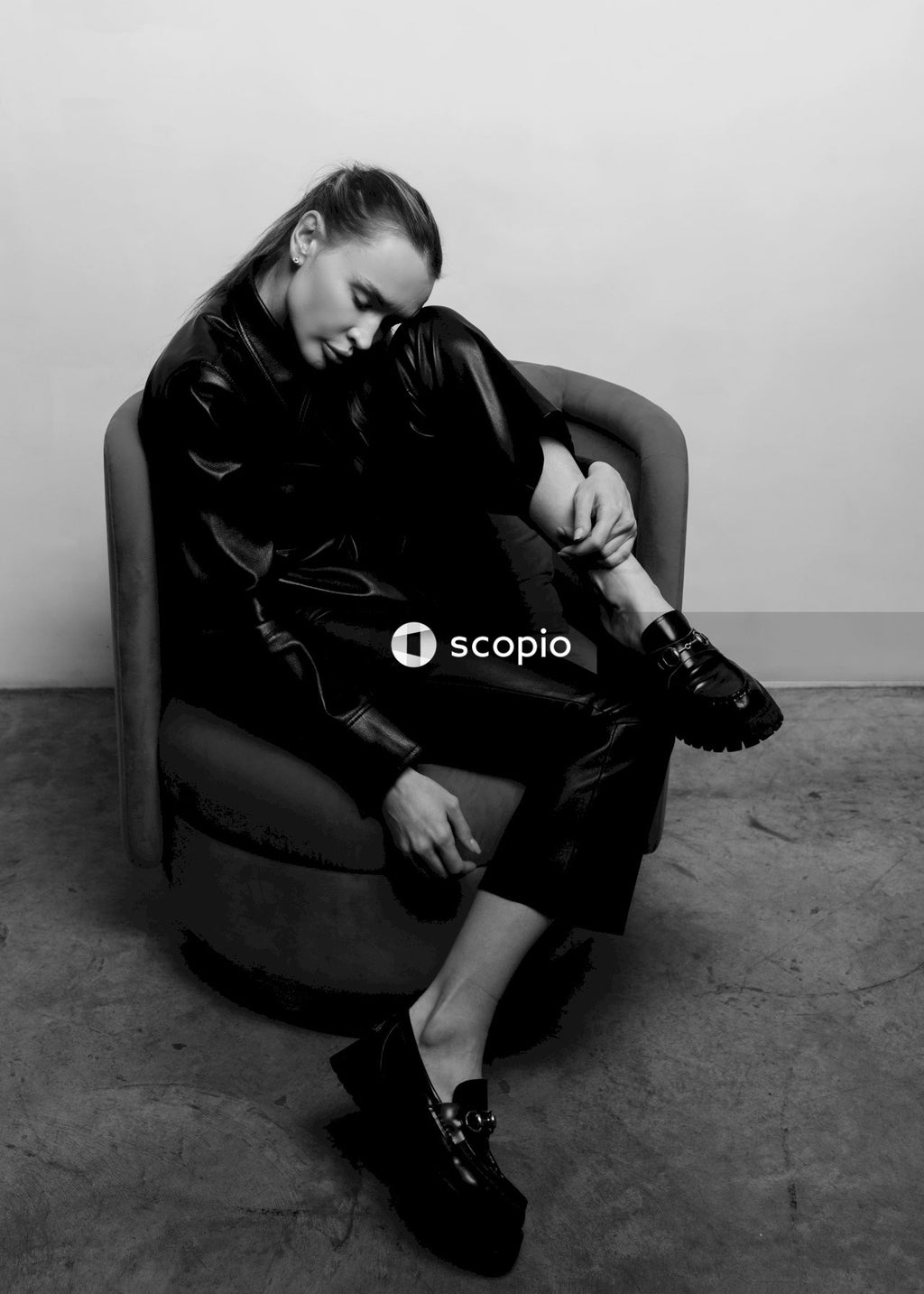 Woman in black leather jacket sitting on black leather armchair
