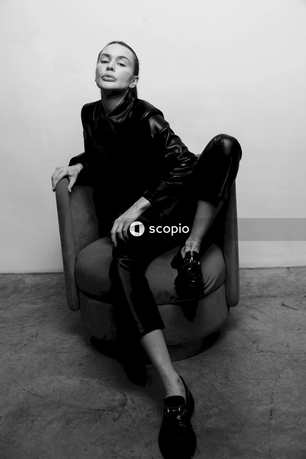 Woman in black leather jacket sitting on gray sofa chair