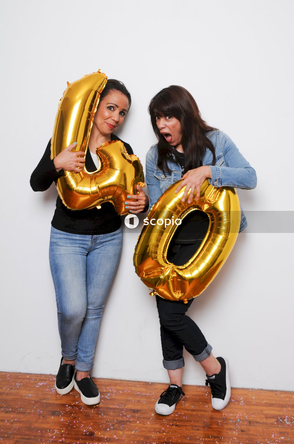 Woman in black long sleeve shirt hugging woman in blue denim jeans holding gold heart shaped