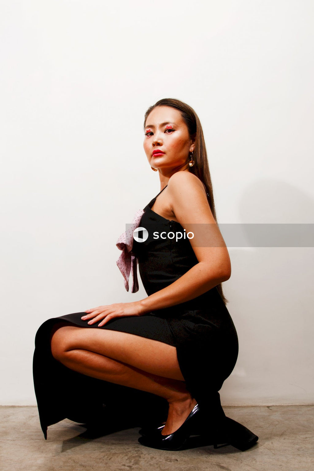 Woman in black sleeveless dress sitting on white floor