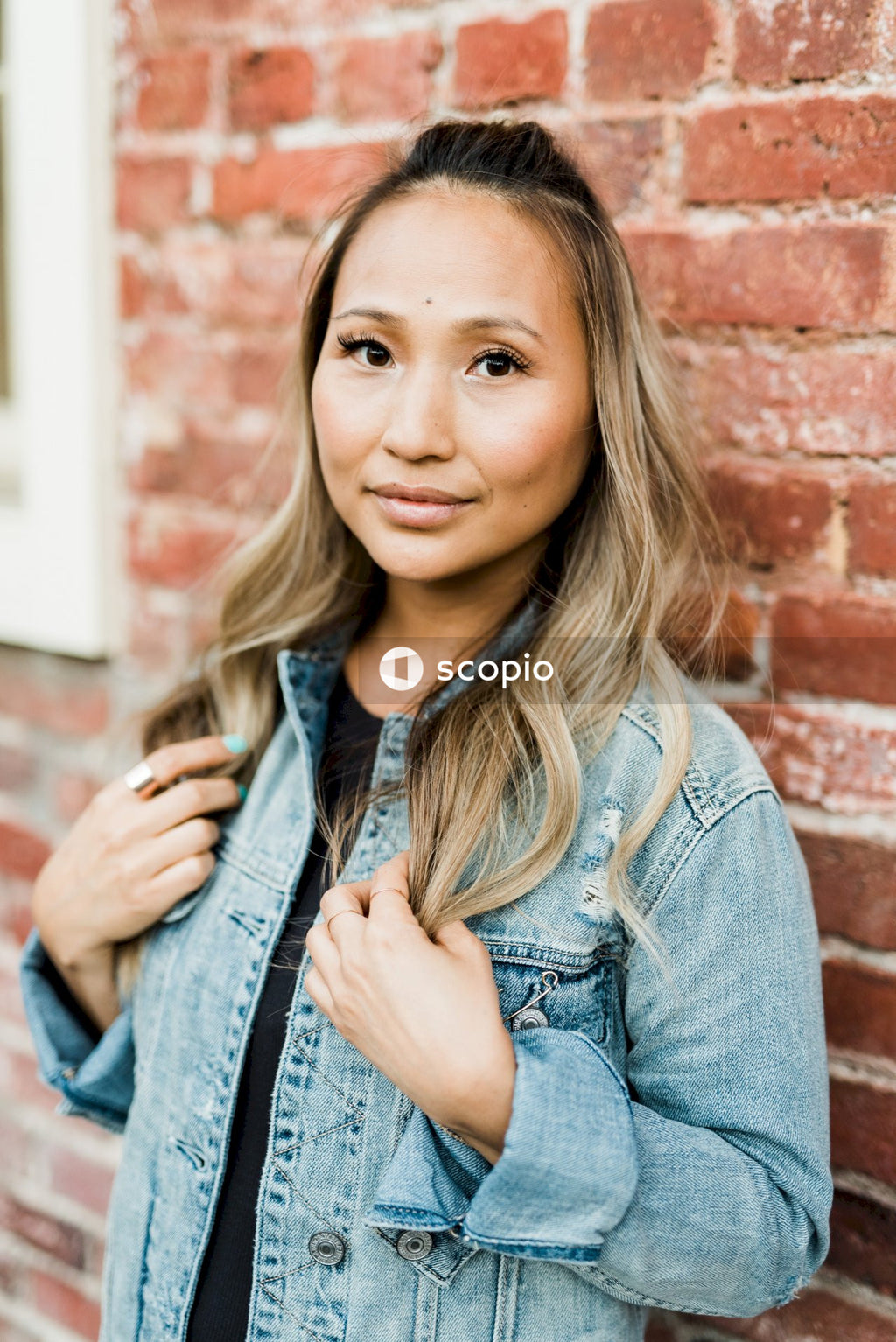 Woman in blue denim jacket leaning on brown brick wall