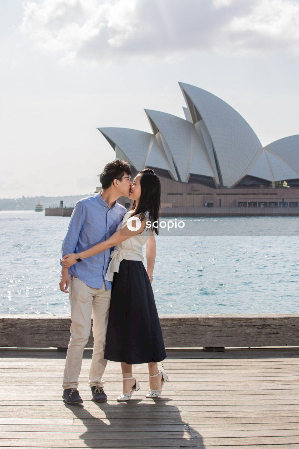 Man and woman kissing and standing on a dock beside Sydney's Opera House