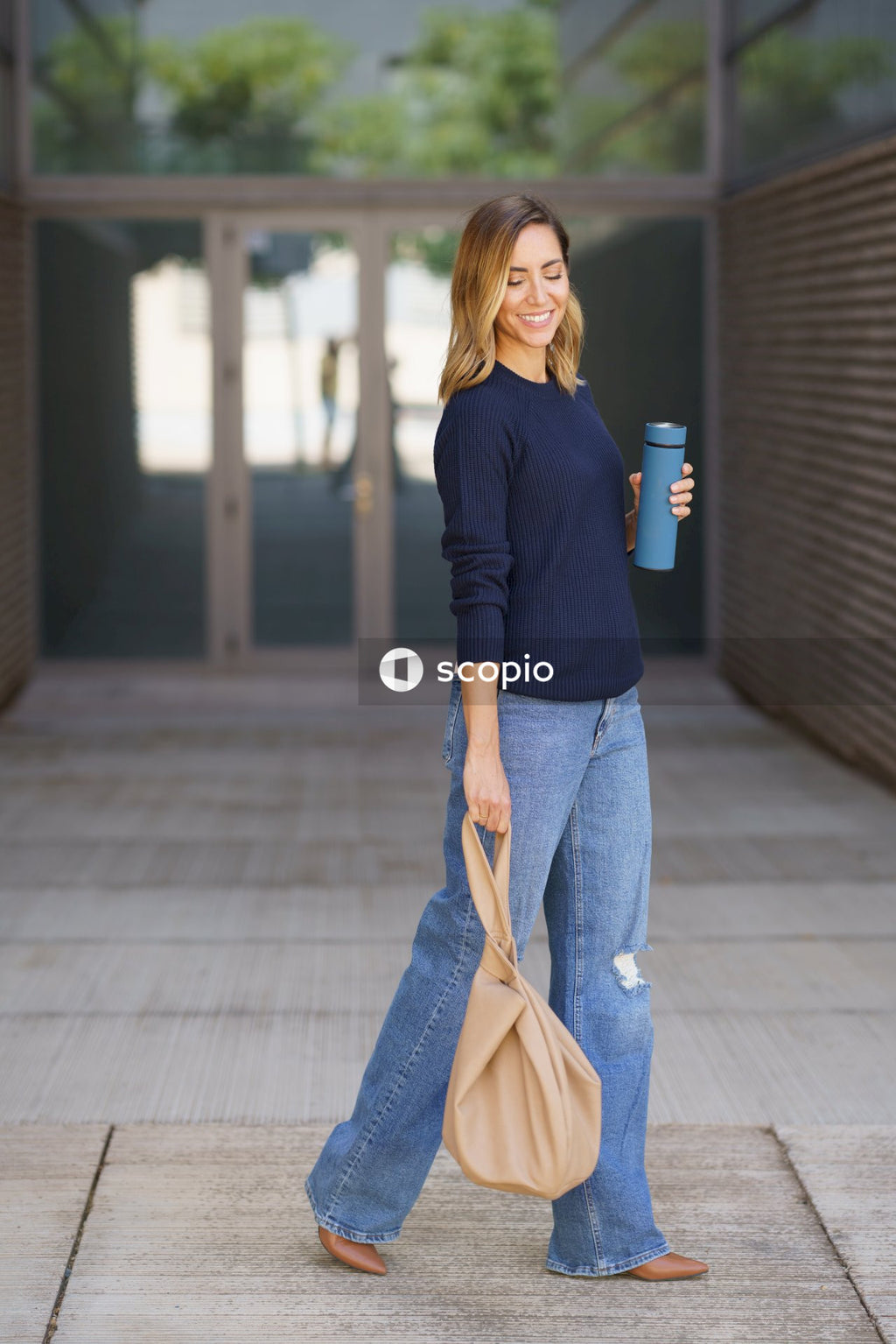 Woman in blue long sleeve shirt and gray pants holding brown leather sling bag