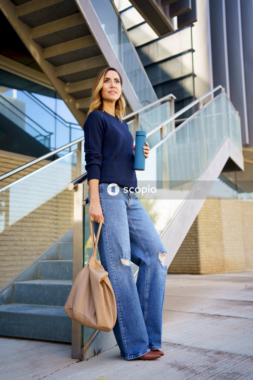 Woman in blue long sleeve shirt and gray pants standing on white staircase